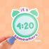 A die cut sticker of a mint green alarm clock with the time that reads 4:20. Purple lettering above and below the clock make the message spell out "it's 4:20 somewhere"