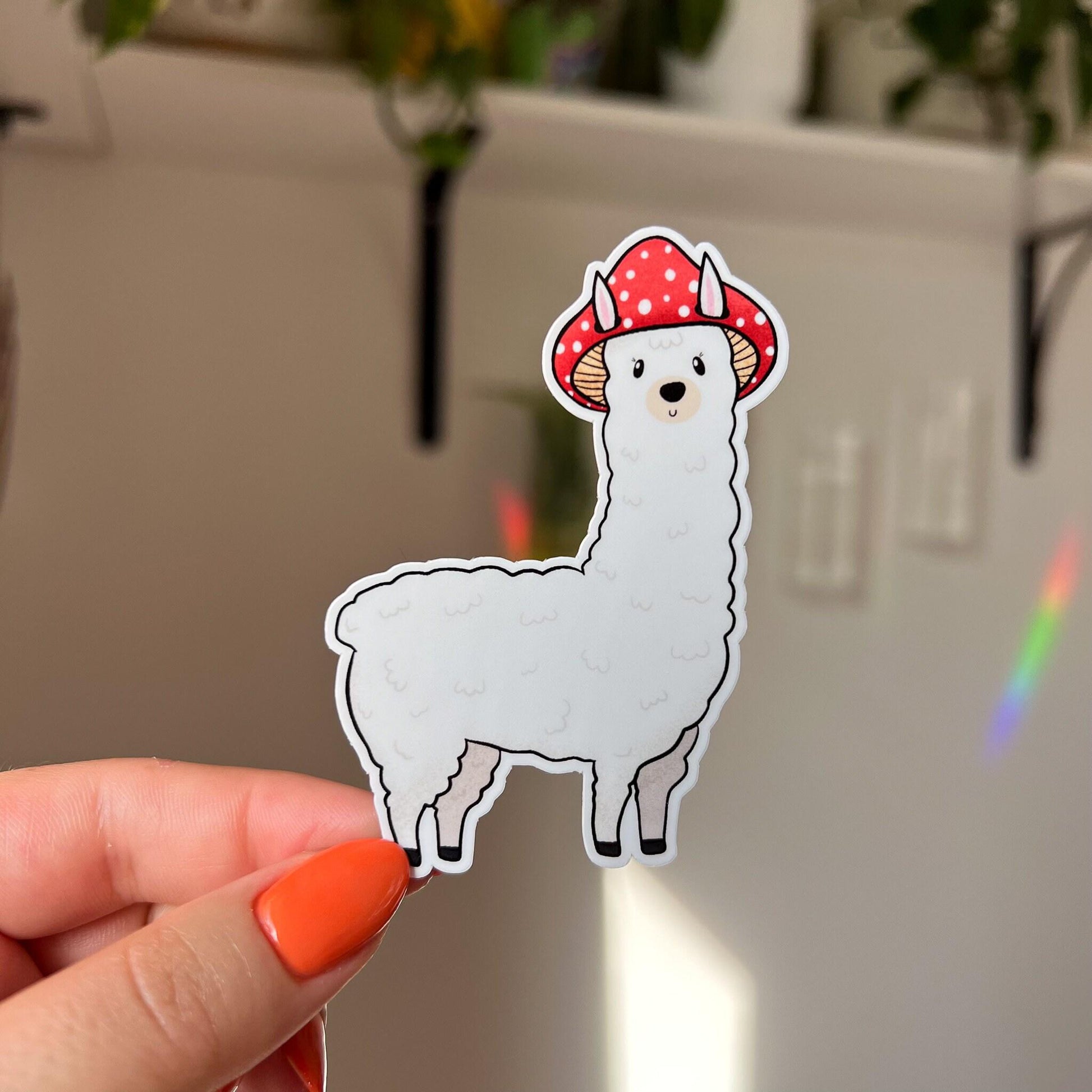A die cut sticker of a white alpaca wearing a red mushroom cap