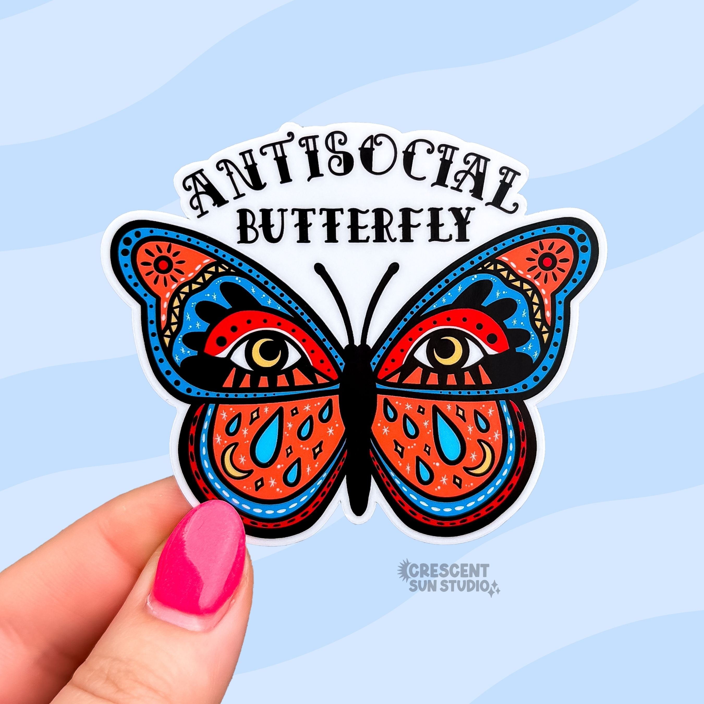 Die cut sticker of a boldly illustrated butterfly with large eyes on its wings and celestial details including moons, teardrops, and suns, with 'Antisocial Butterfly' arched above in decorative lettering.