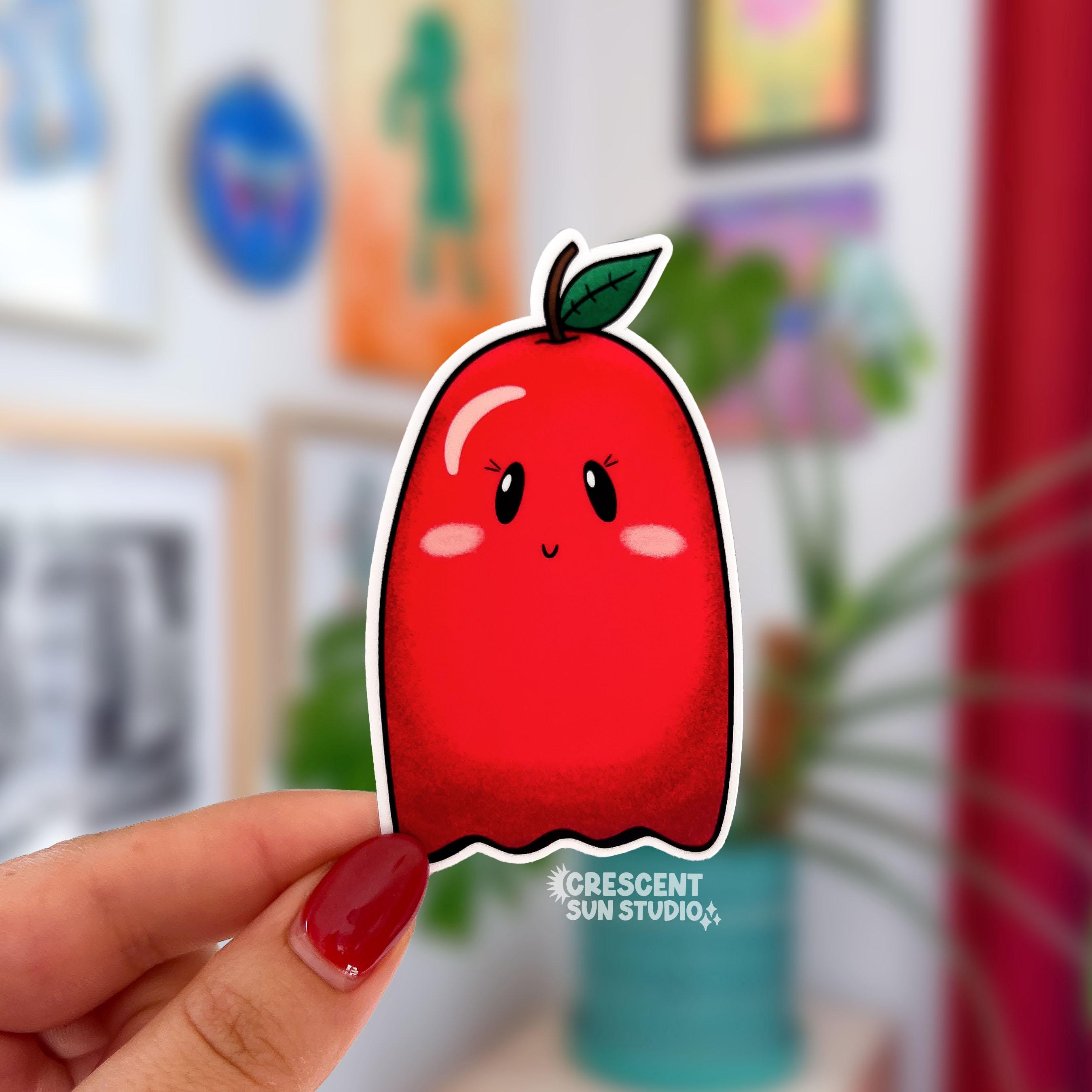 A die cut sticker of a pink cheeked red apple ghost character.