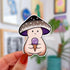 A mushroom character sticker whose cap is shades of black and grey with a purple underside. The mushroom holds a purple ice cream cone.