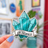 A sticker in the shape of three turquoise shaded crystals. At the bottom is a white banner with black text that reads "I attract abundance"