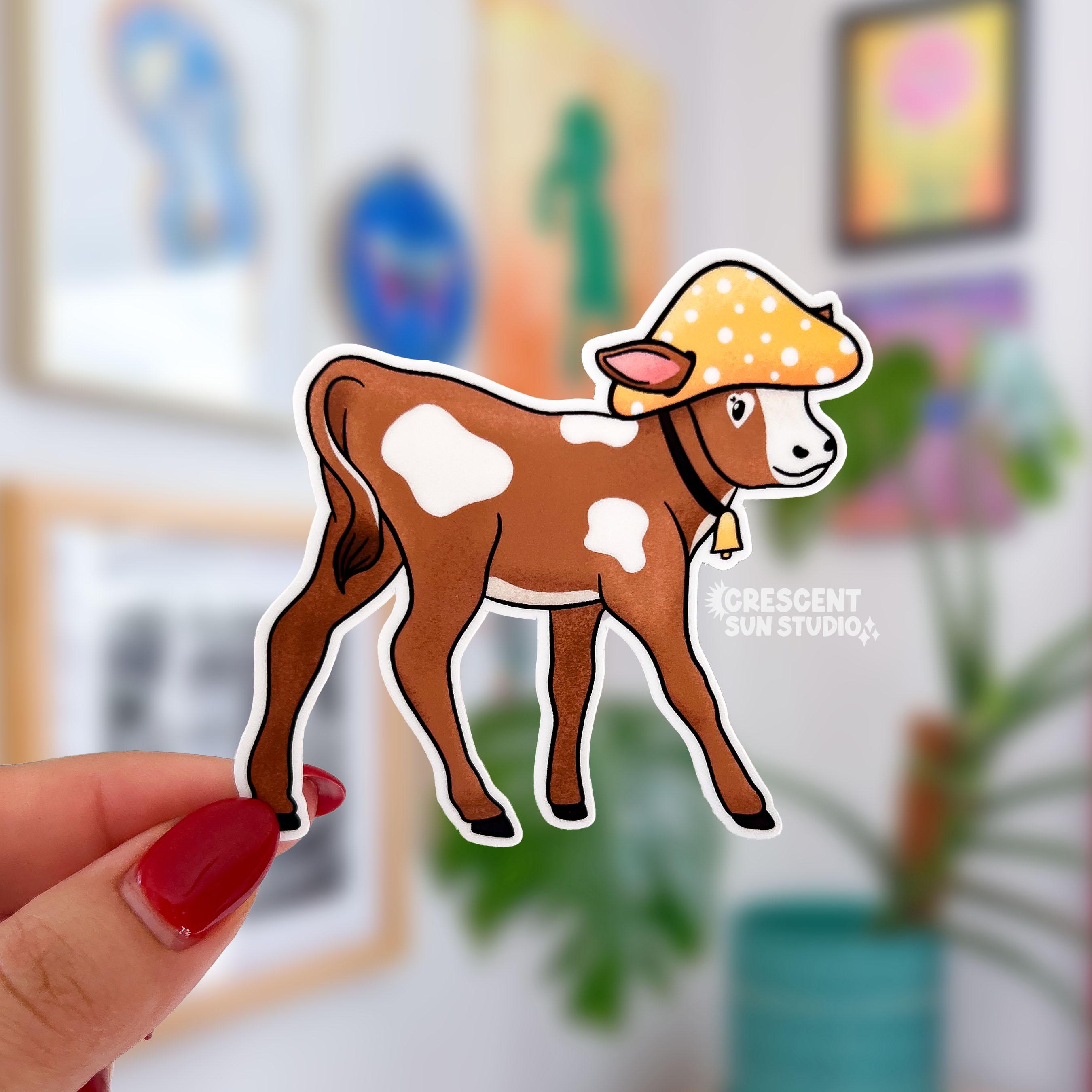A brown and white baby cow wears a yellow mushroom hat in this die cut sticker.