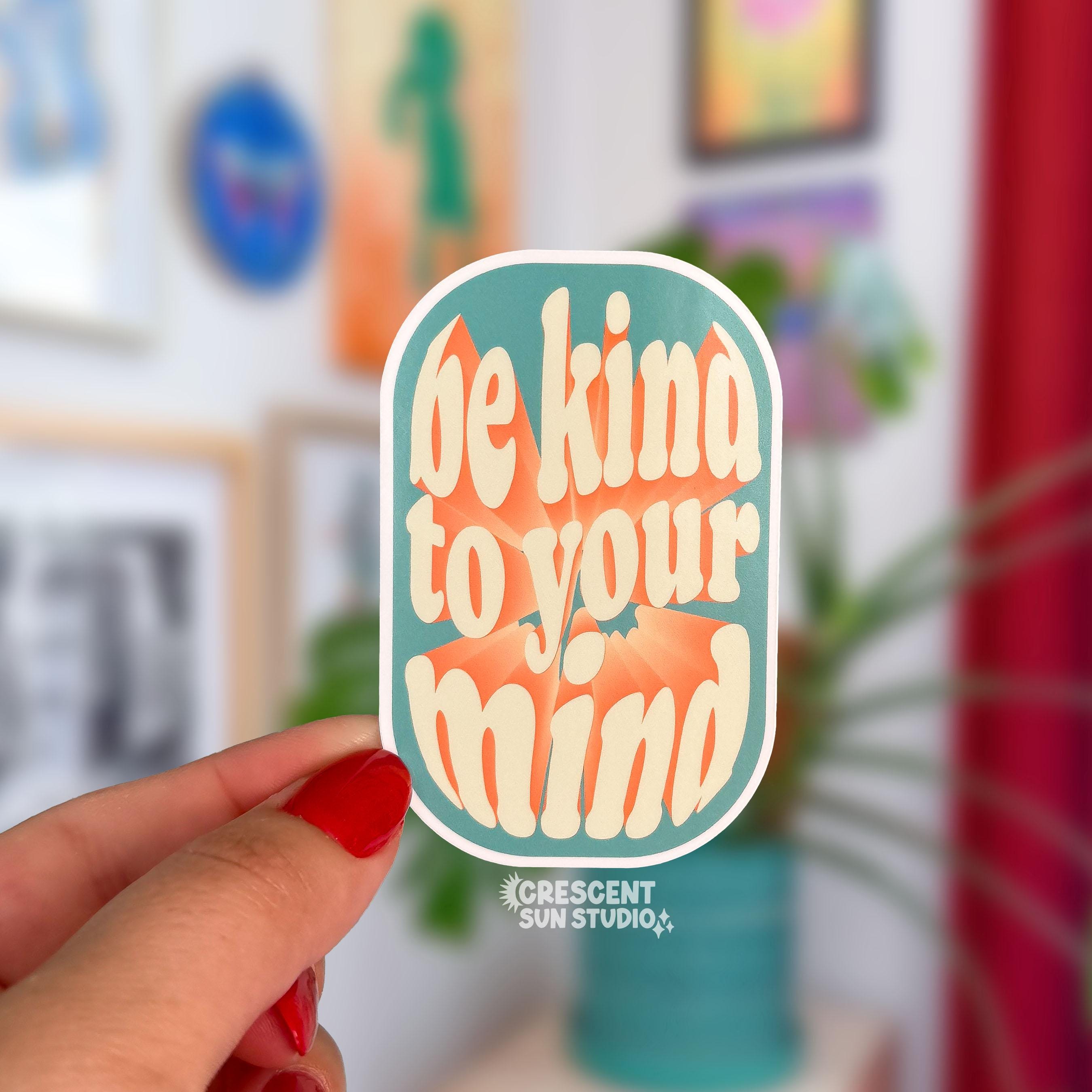 Die-cut sticker with a teal rounded rectangle background reading 'be kind to your mind' in cream retro lettering with an orange accent
