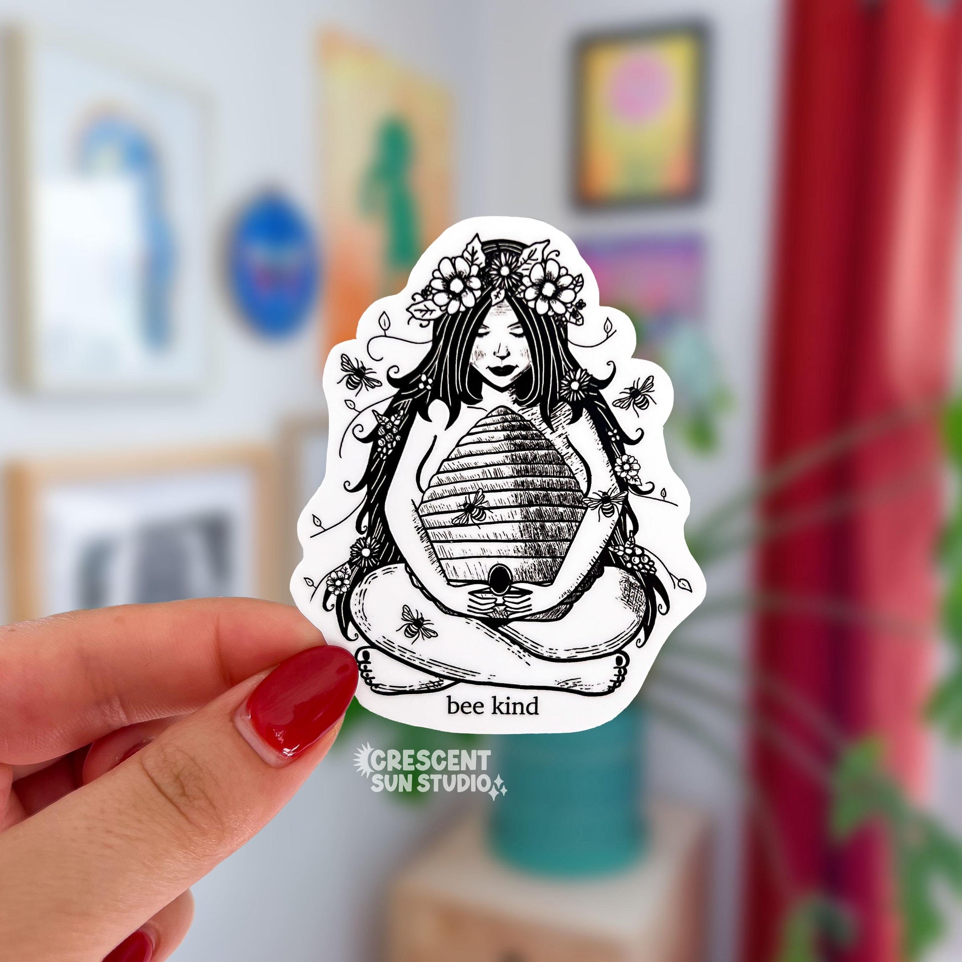 This is a die cut black and white sticker of a nature goddess sitting with her legs crossed and cradling a bee hive.