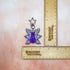 A purple cat with one large pink eye at the center of its face stoically observes you. The cat has three pairs of light-colored angel wings, each wing covered with watchful pink eyes. 

The key chain connects to your favorite things via a star shaped clasp.

This image shows the keychain next to two rulers, showing its size of 2.25 in x 2.25 in