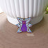 A pin leans against a white pot. The pin is of a purple cat with one large pink eye at the center of its face stoically observes you. The cat has three pairs of light-colored angel wings, each wing covered with watchful pink eyes. 
