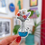 a die cut sticker of a bong with blue water being used as a vase for a variety of wildflowers