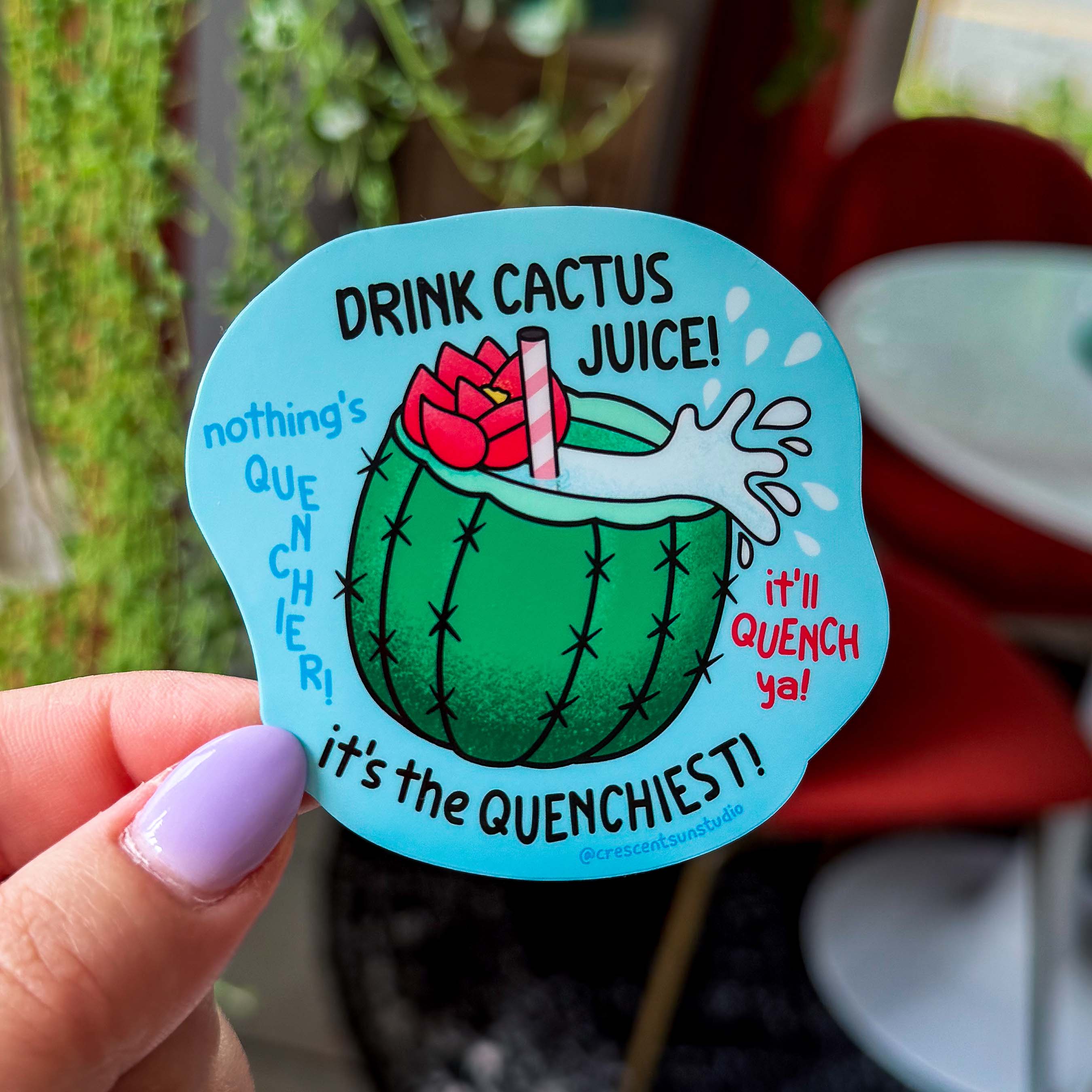 A blue die cut sticker of a cactus cup with a straw, red flower, and cactus juice surrounded by the quotes, "drink cactus juice," "nothing's quenchier," "it's the quenchiest," and "it'll quench ya!"