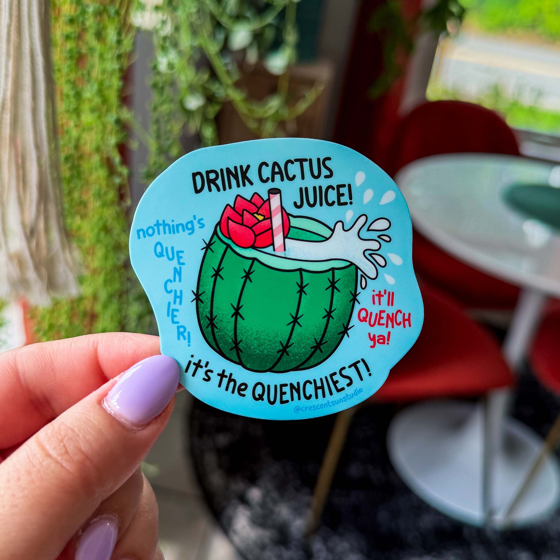 A blue die cut sticker of a cactus cup with a straw, red flower, and cactus juice surrounded by the quotes, "drink cactus juice," "nothing's quenchier," "it's the quenchiest," and "it'll quench ya!"