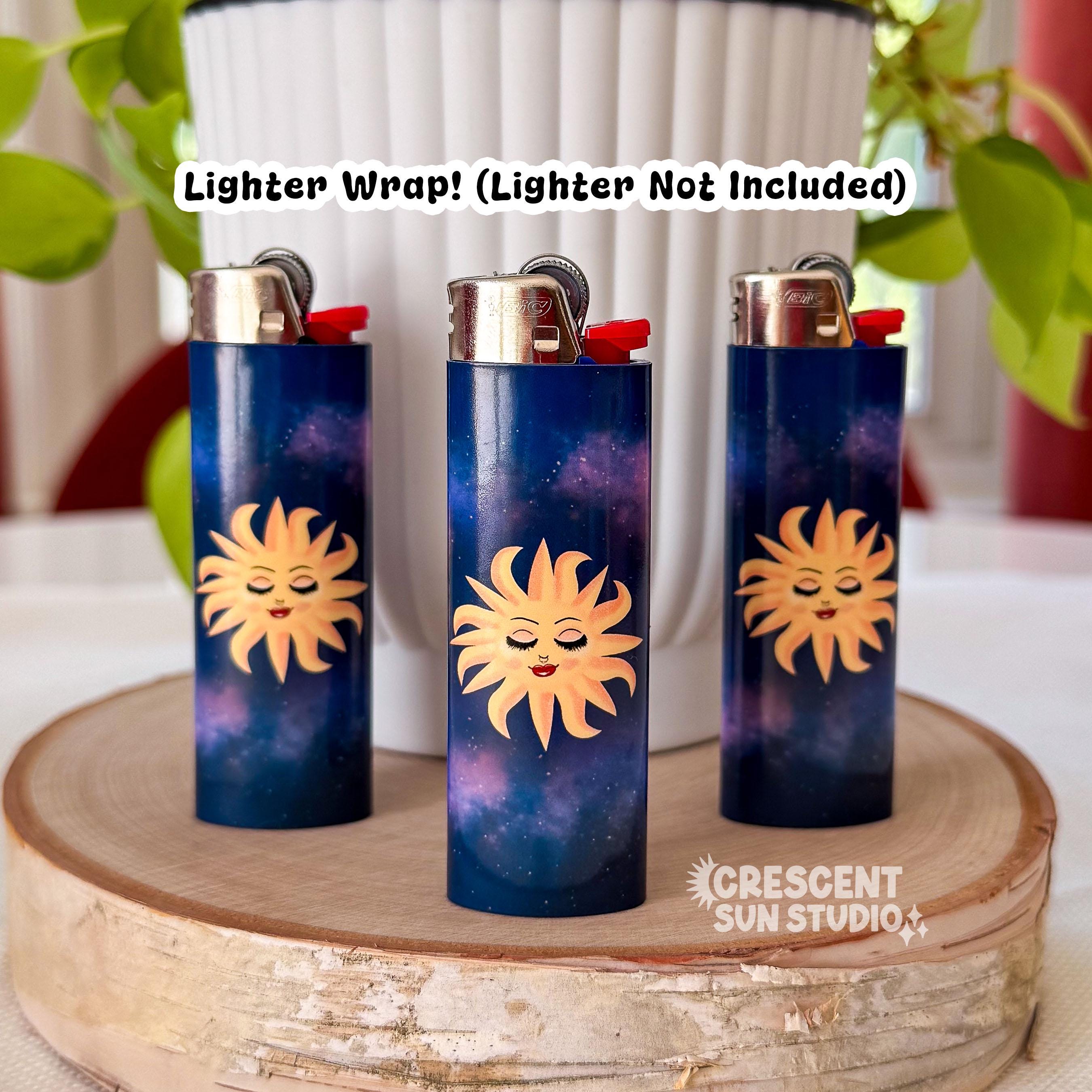 This lighter wrap features a blissed out and elevated glam sun floats in a purple-blue galaxy background. This personified sun has thin eyebrows, closed eyes with full lashes and eyeshadow, a nose ring, blushing cheeks, and glossy full lips.

In this image, three lighters, each wrapped in a lighter wrap, stand on a wooden display. 

Across the image, the text reads "Lighter wrap! Lighter not included."