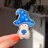 A sticker in the shape of a wizard mushroom character. The mushroom cap is blue with white stars and spirals. The magician holds a 20-sided die, used in tabletop games, and has rolled a 1. You can tell from his face that he's sad about it.