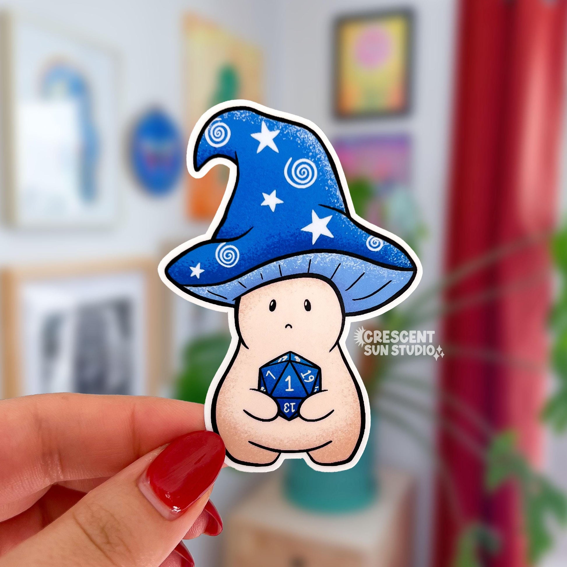 A sticker in the shape of a wizard mushroom character. The mushroom cap is blue with white stars and spirals. The magician holds a 20-sided die, used in tabletop games, and has rolled a 1.