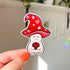 This sticker is shaped like a happy mushroom character whose cap is shaped like a red wizard's hat holds a d20 die. In this image, a hand holds the sticker close to the camera.