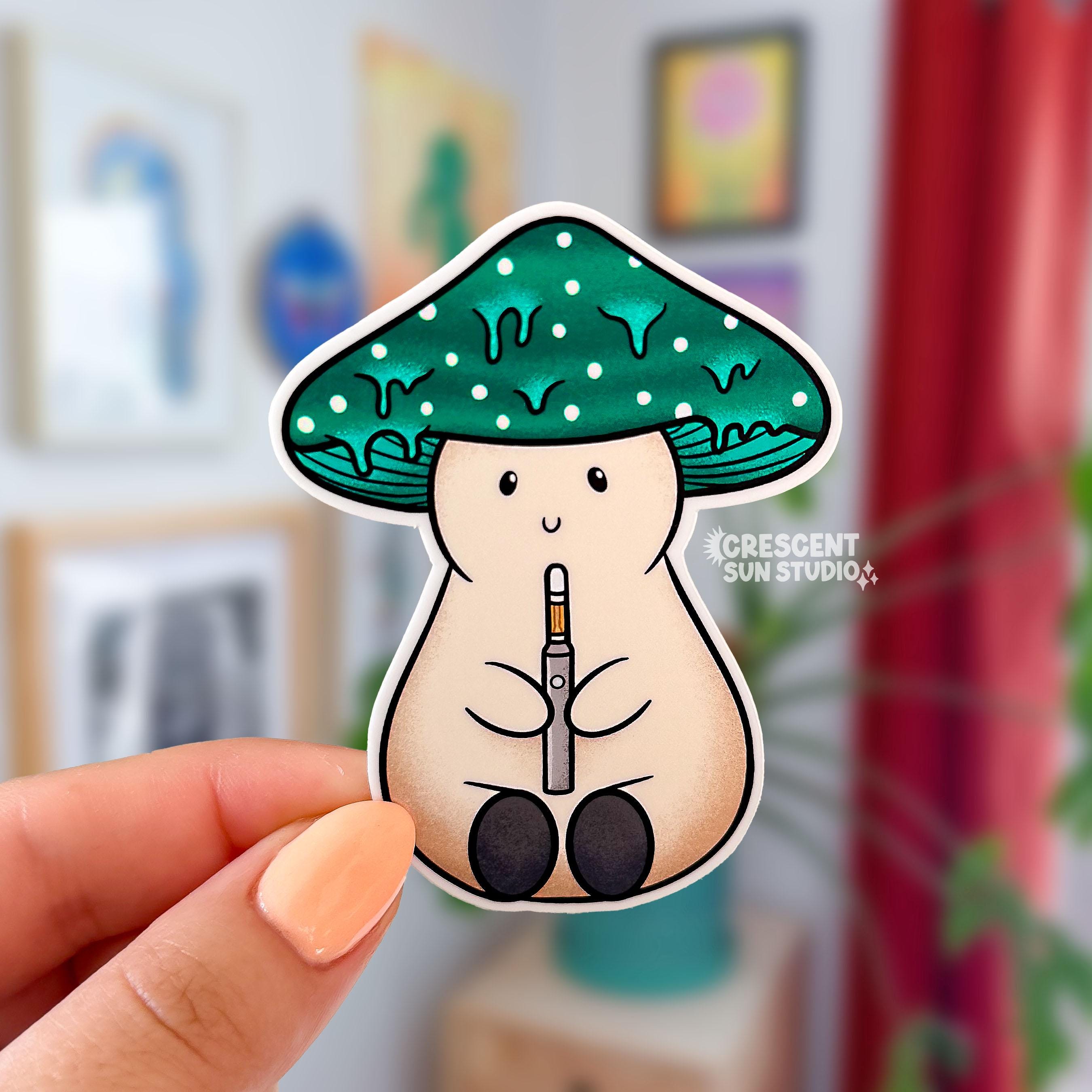 A sticker in the shape of a beige plump mushroom character with a dark teal dripping cap with white spots, holding a dab pen. The mushroom has a smiling face.