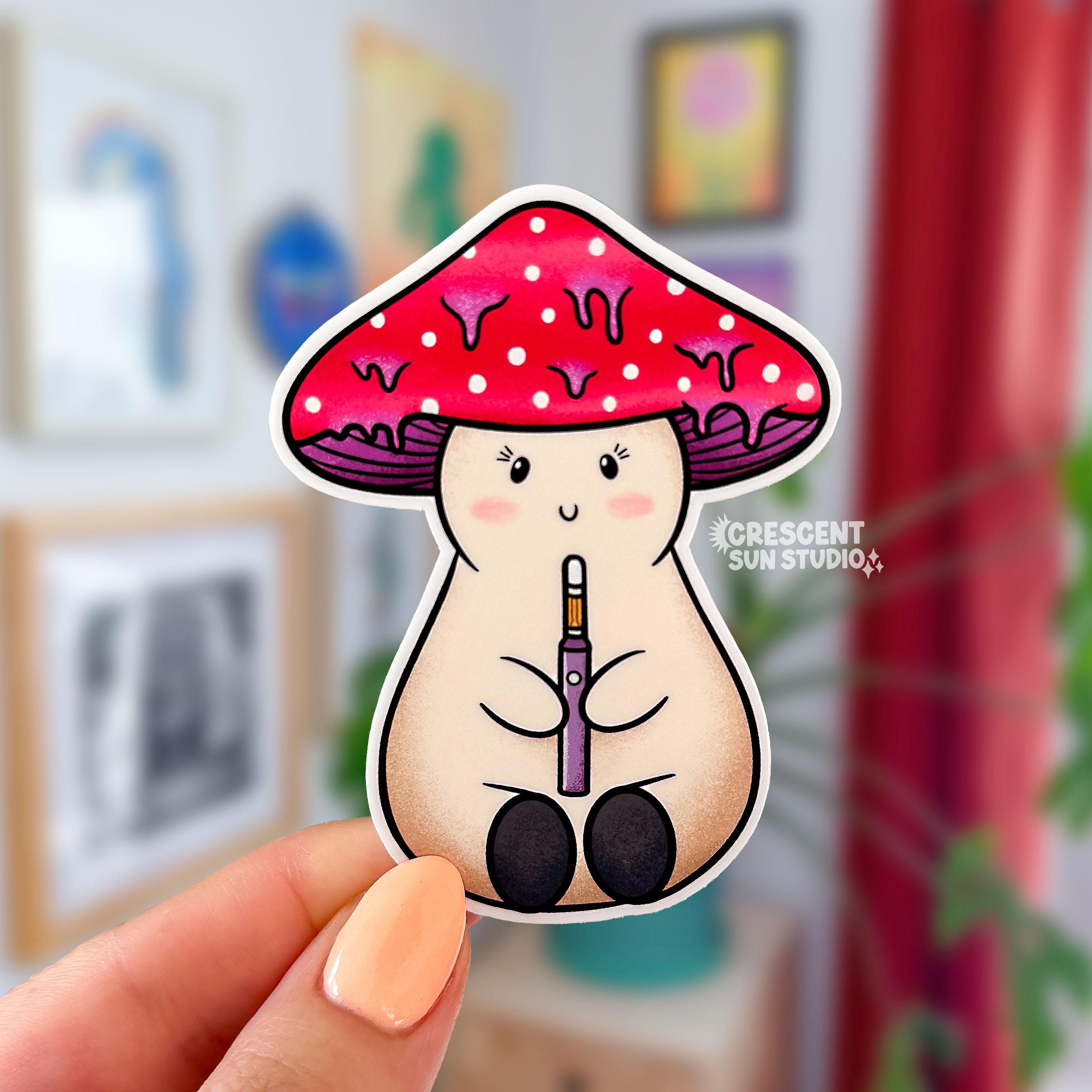 A die cut sticker of a beige stoner girl mushroom character holding a dab pen. She is smiling, has eyelashes and pink cheeks. Her mushroom cap is red and white with purple drips.