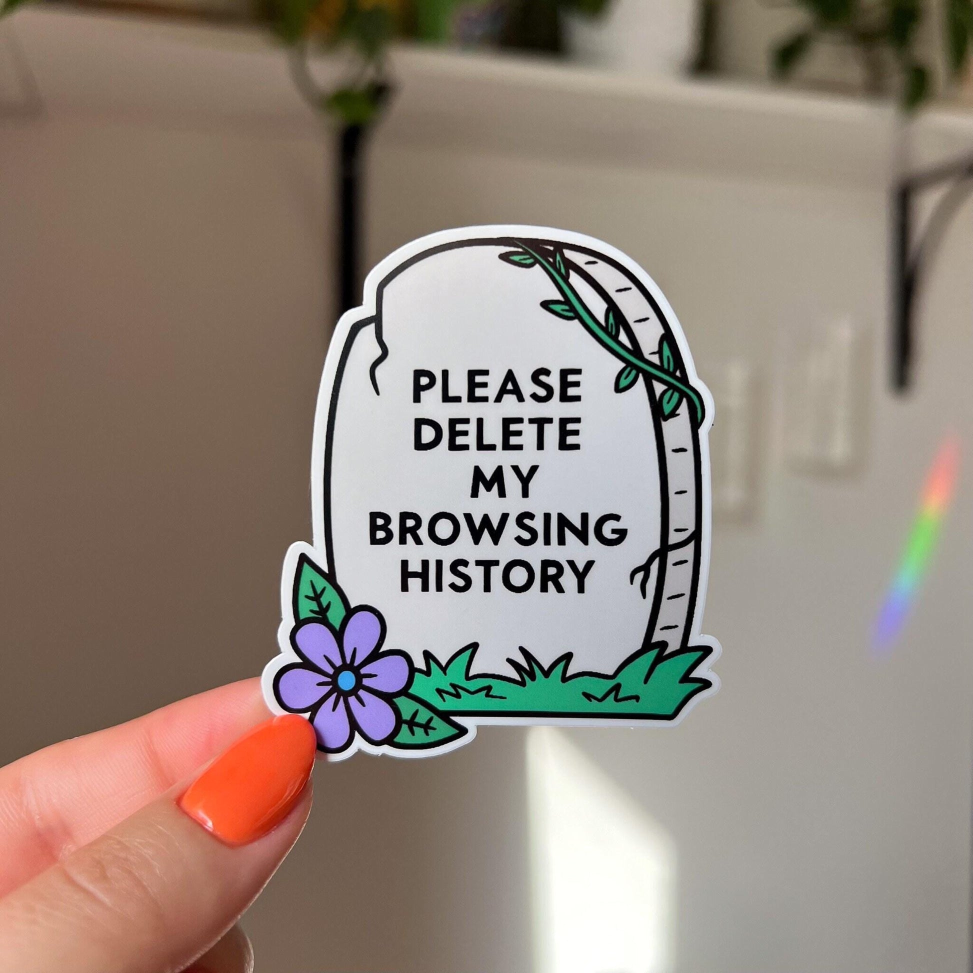 A light grey gravestone sticker with the text that reads "please delete my browsing history" in black. There is a purple daisy on the bottom left corner.