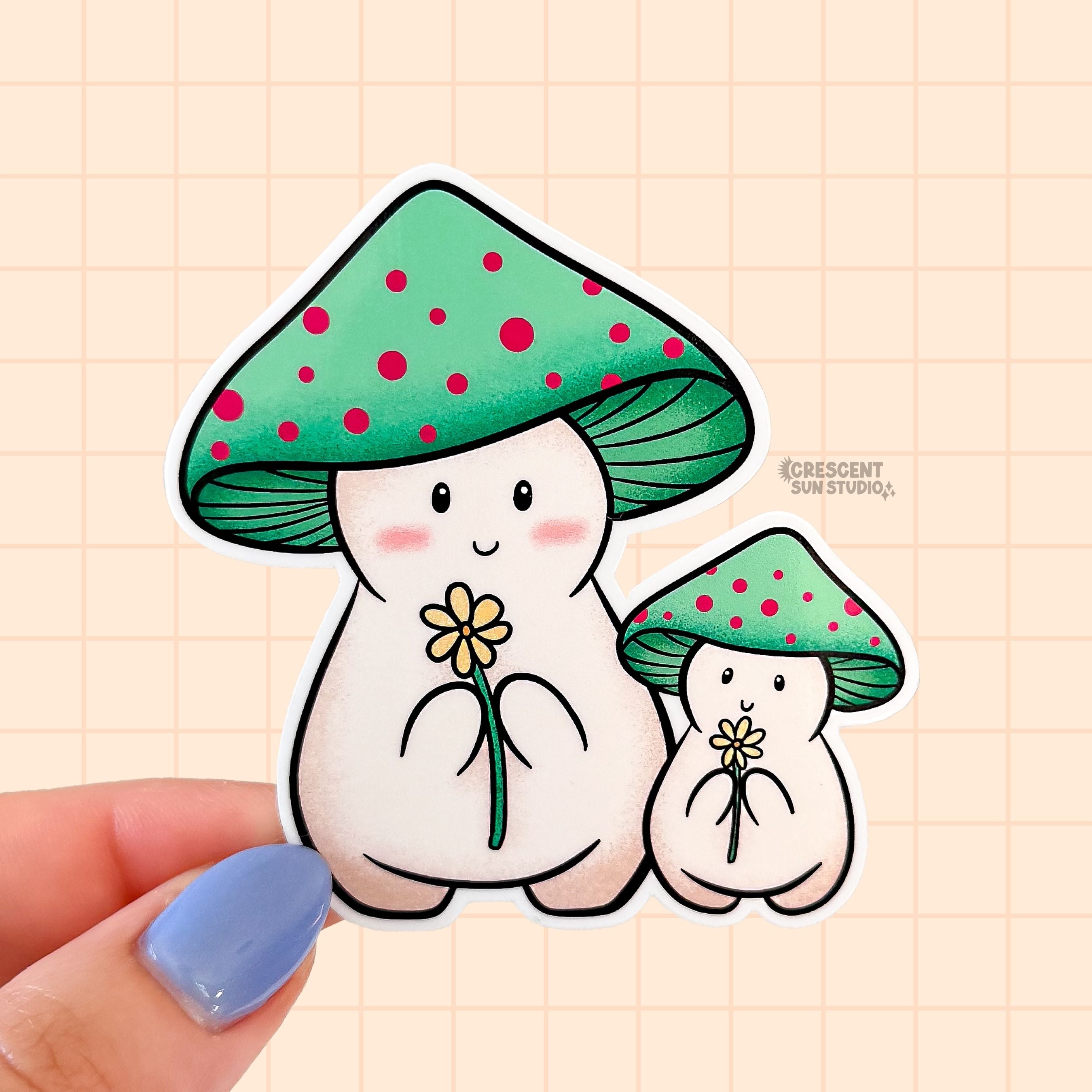 A sweet die cut sticker of two mushroom characters. Both have green mushroom caps with red spots. They are both light beige and holding a yellow daisy. One mushroom is smaller than the other, indicating a child. 