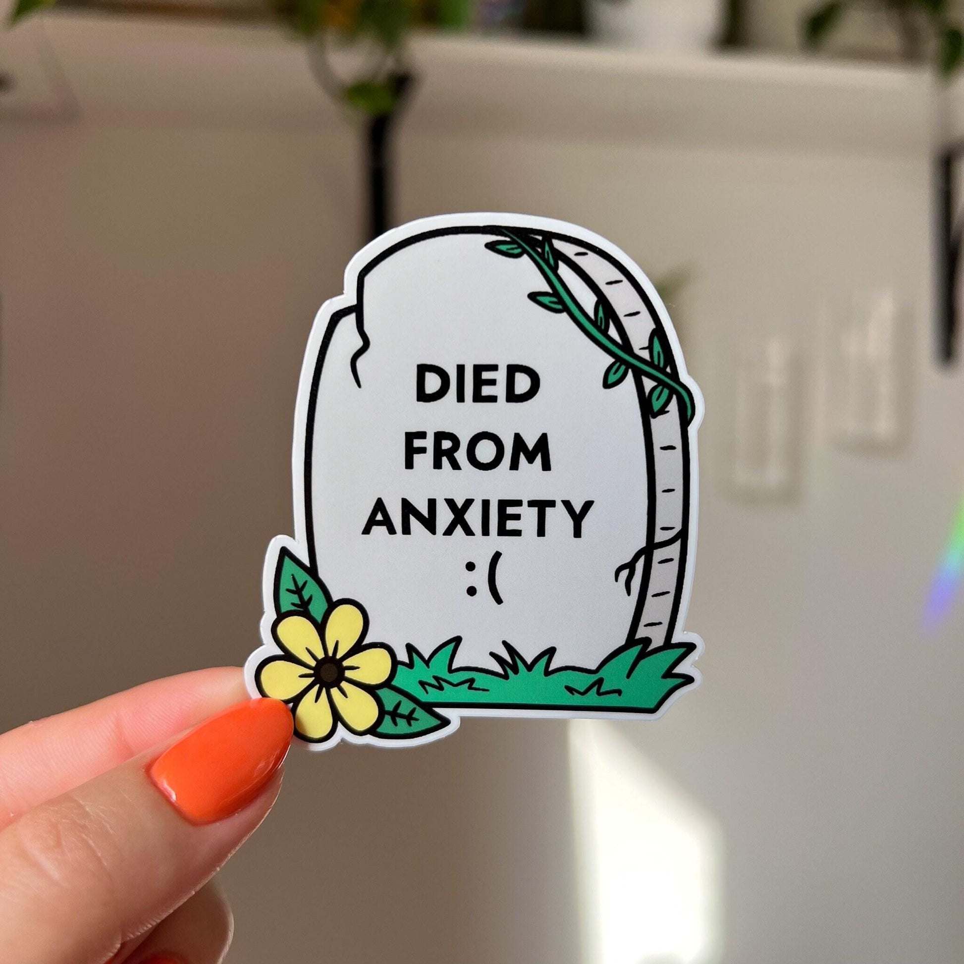 A light grey tombstone shaped sticker reads "died from anxiety :(" with a yellow flower in the bottom left corner.