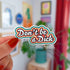 die cut sticker of "don't be a dick" in white script text surrounded by outlines of orange, yellow and teal.