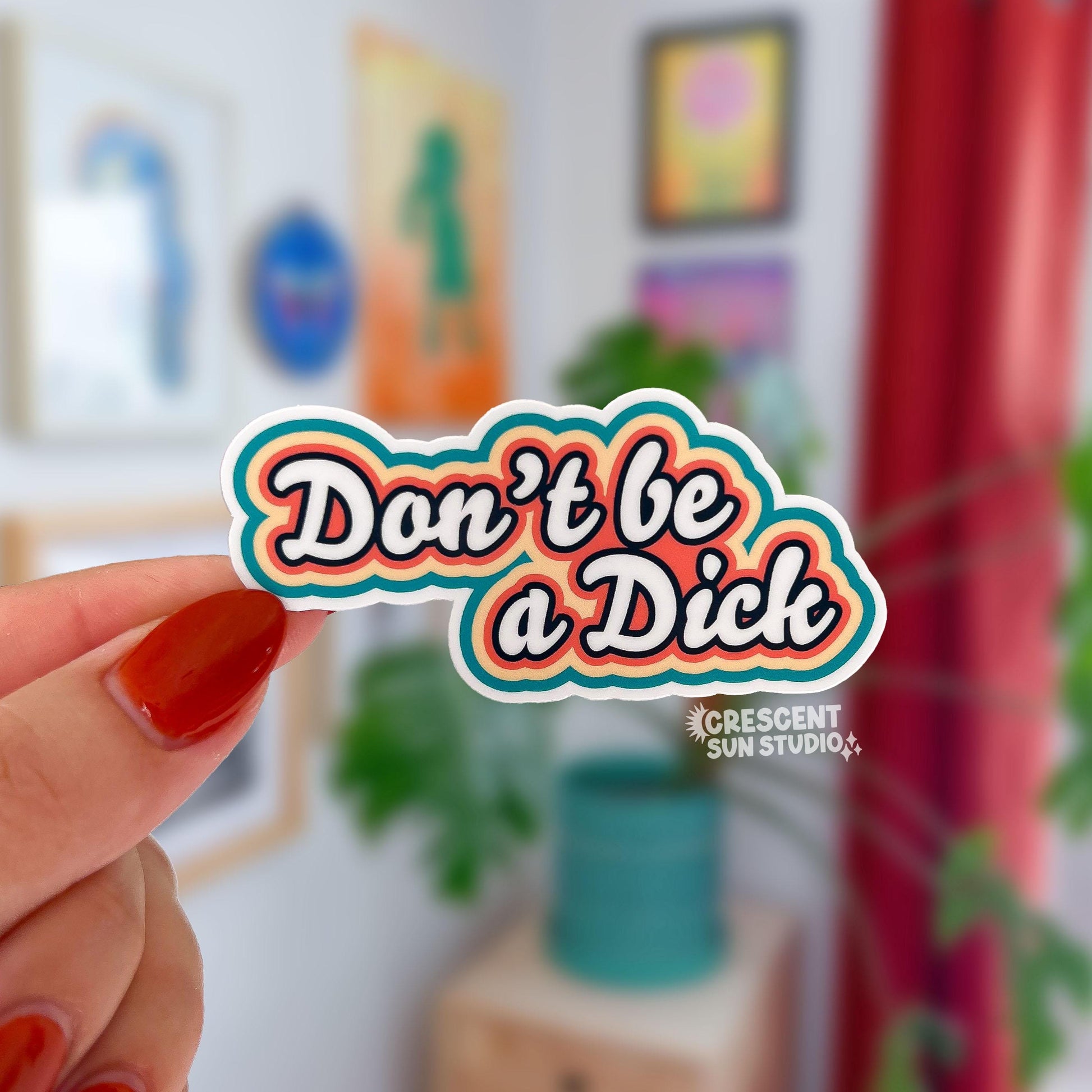 die cut sticker of "don't be a dick" in white script text surrounded by outlines of orange, yellow and teal.
