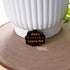 Leaning against a white pot is a black cloud shaped pin with gold lettering that reads "don't fucking touch me" surrounded by little stars.