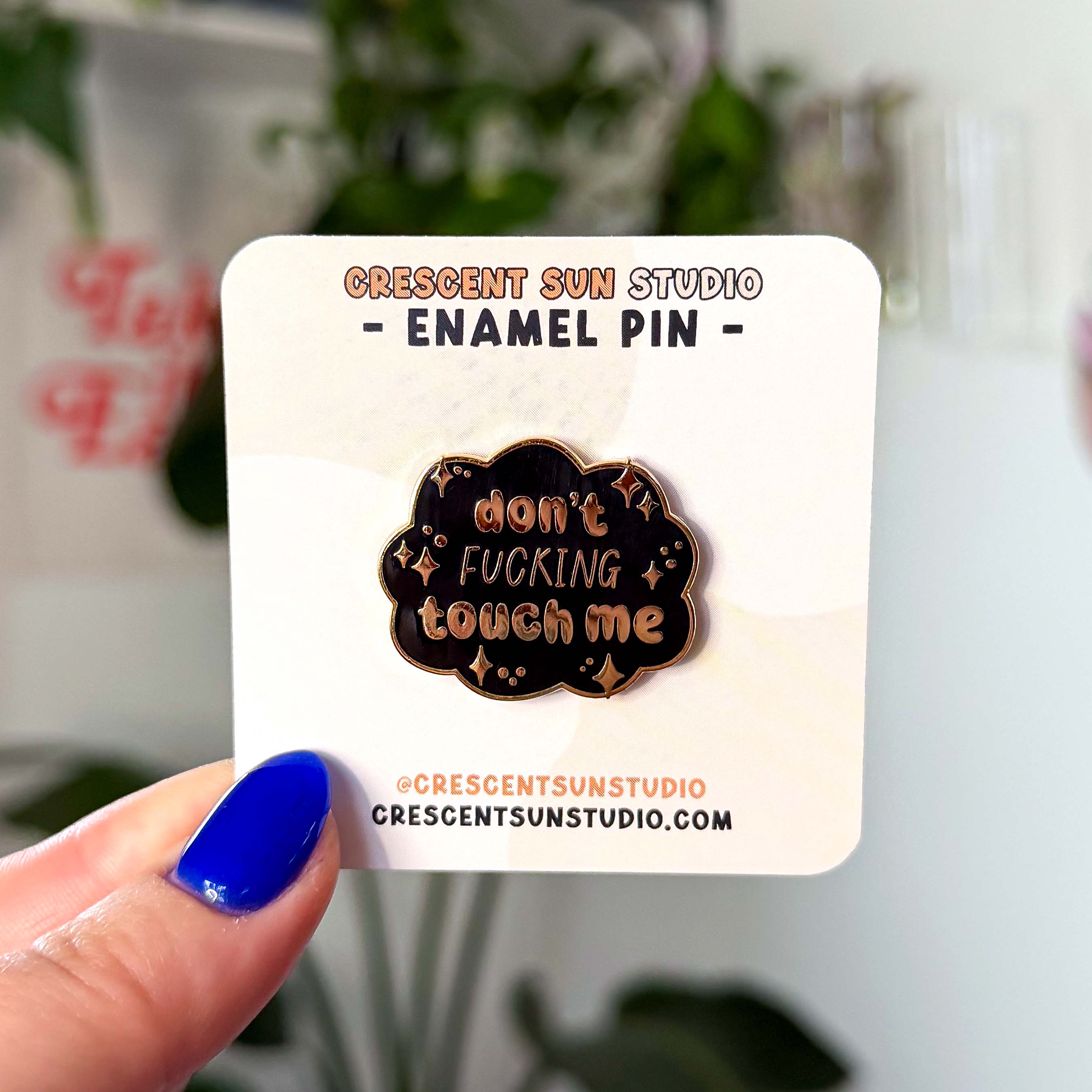 A black cloud shaped pin with gold lettering that reads "don't fucking touch me" surrounded by little stars.