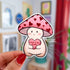 Dovey is a happy and plump cream mushroom character wearing a pink cap with red hearts. They are holding a pink candy heart that reads "Love U So Mush" in red lettering.