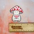 Dovey is a happy and plump cream mushroom character wearing a pink cap with red hearts. They are holding a pink candy heart that reads "Love U So Mush" in red lettering. 

This image shows the Dovey magnet above a wooden ruler, showing its size of 2.3 x 2.8 inches.