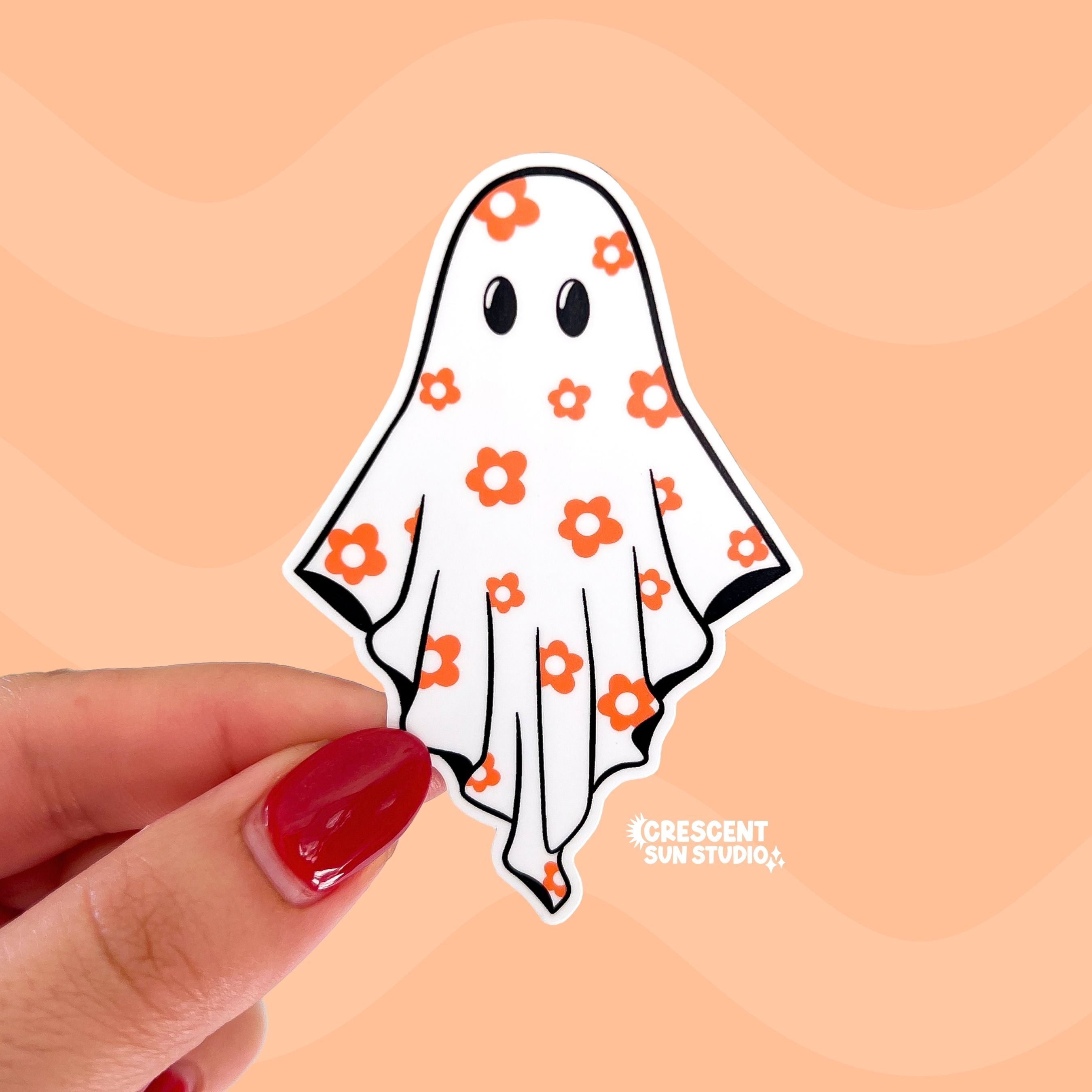 Hand holding a ghost-shaped sticker with floral patterns