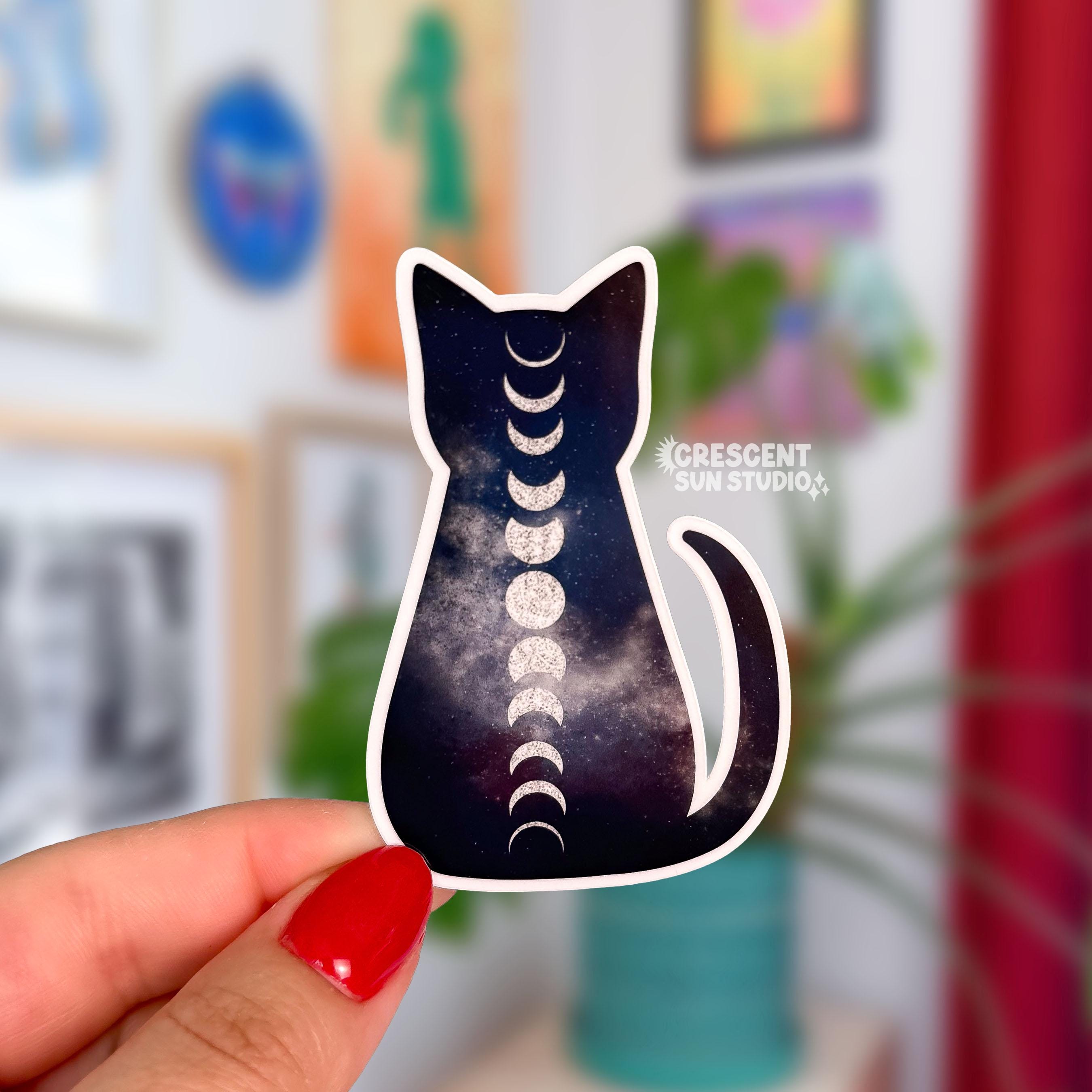 A sticker in the shape of a cat silhouette. The cat is dark in color with a galaxy pattern running through it, with light swirls toward the center. The  also has the moon phases running vertically down its center.