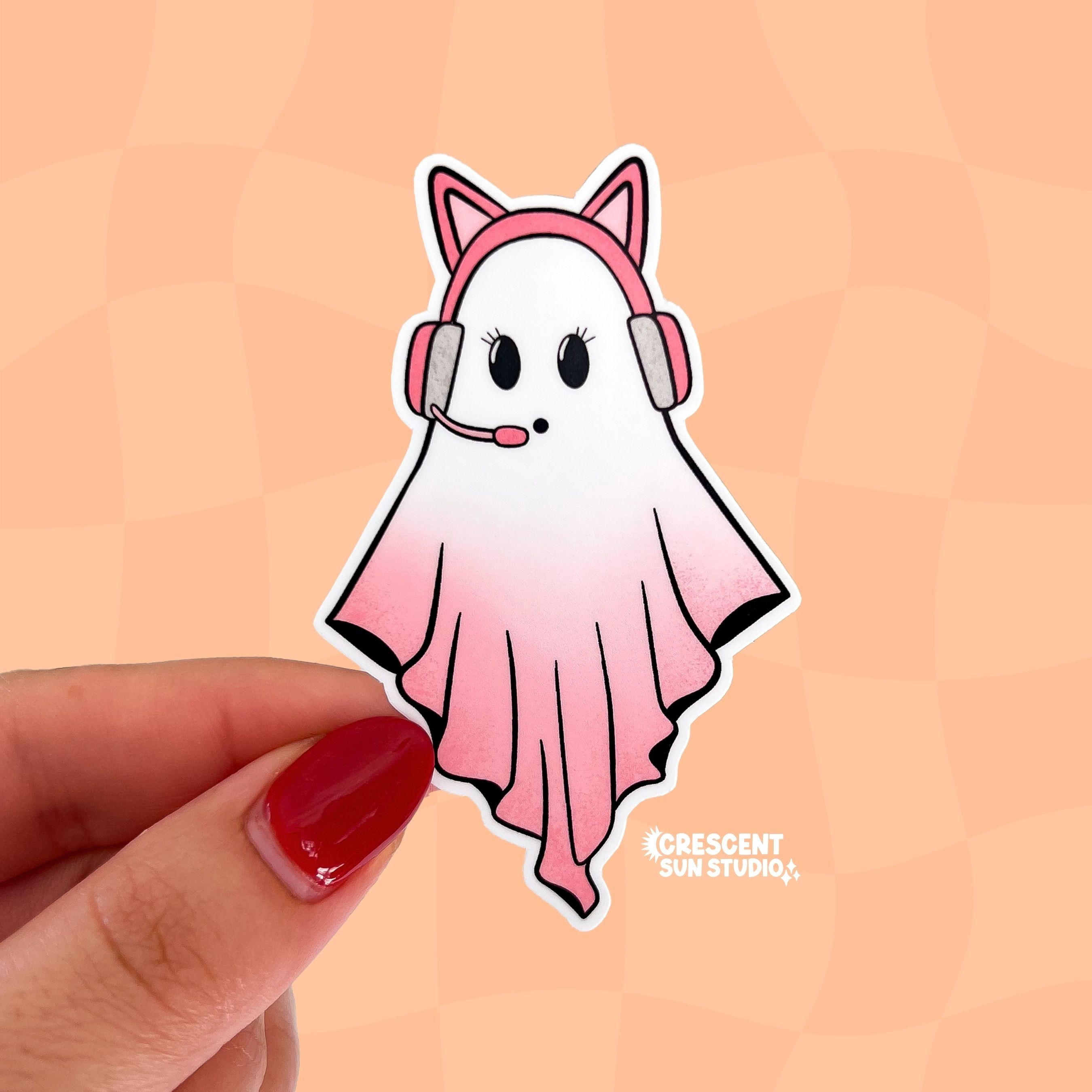 A sticker in the shape of a ghost wearing a pink cat ear headset. Her body is in a gradient pink and white.