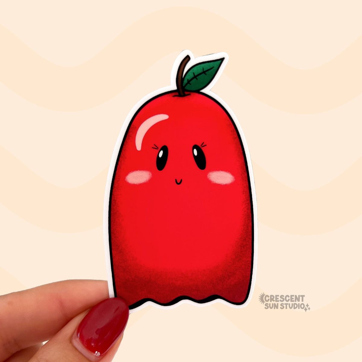 A die cut sticker of a pink cheeked red apple ghost character.