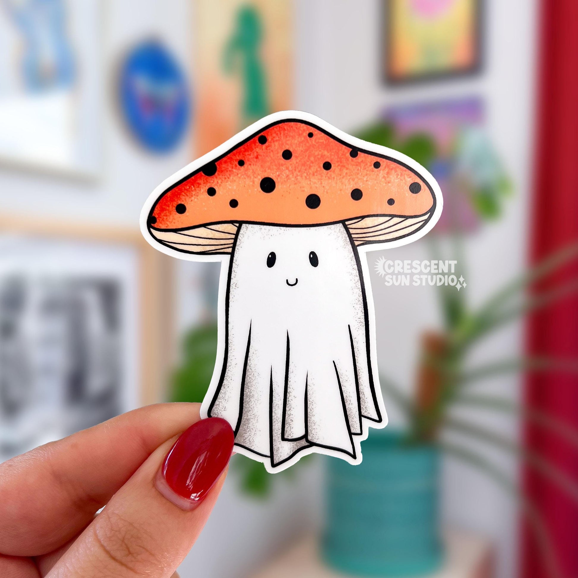 A sticker in the shape of a ghost wearing an orange mushroom top for a hat. The mushroom has dark dots on it and the ghostie has a smiling face.