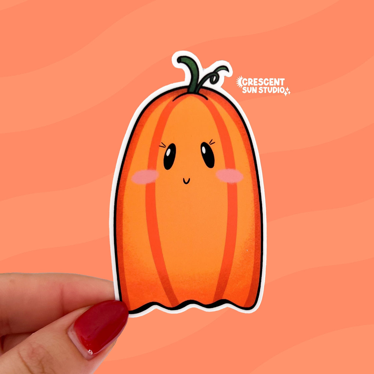 Hand holding a diecut sticker of a cute cartoon ghost that looks like a pumpkin.