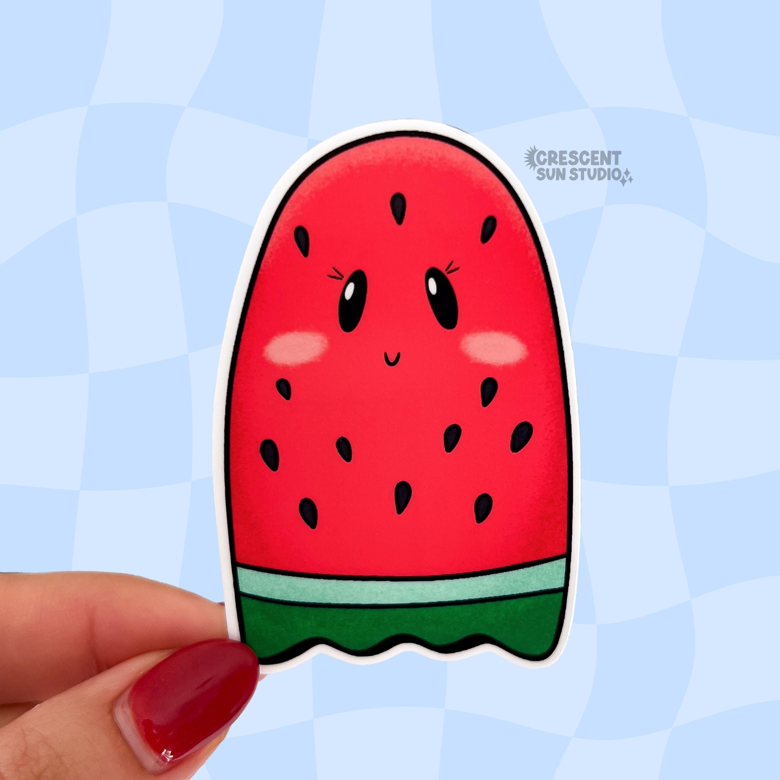 A sticker that looks like a red seeded watermelon slice shaped like a ghost is held close to the camera.