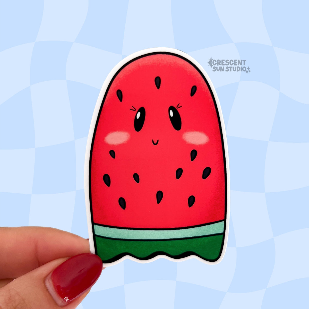 A sticker that looks like a red seeded watermelon slice shaped like a ghost is held close to the camera.