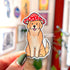 A tan colored golden retriever sticker. The dog sits with his tongue out and wears a red and white mushroom cap.