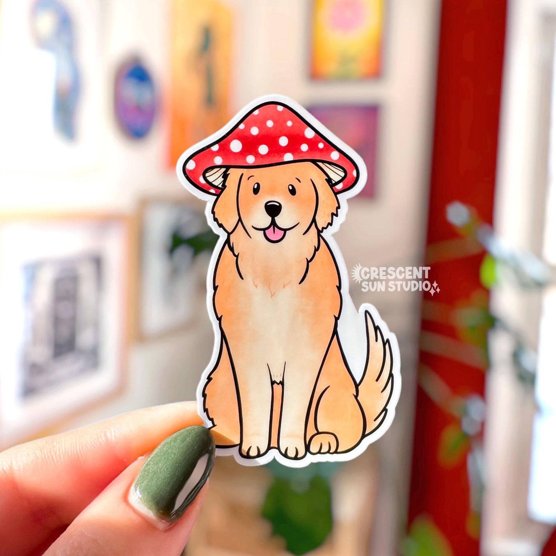 A tan colored golden retriever sticker. The dog sits with his tongue out and wears a red and white mushroom cap.