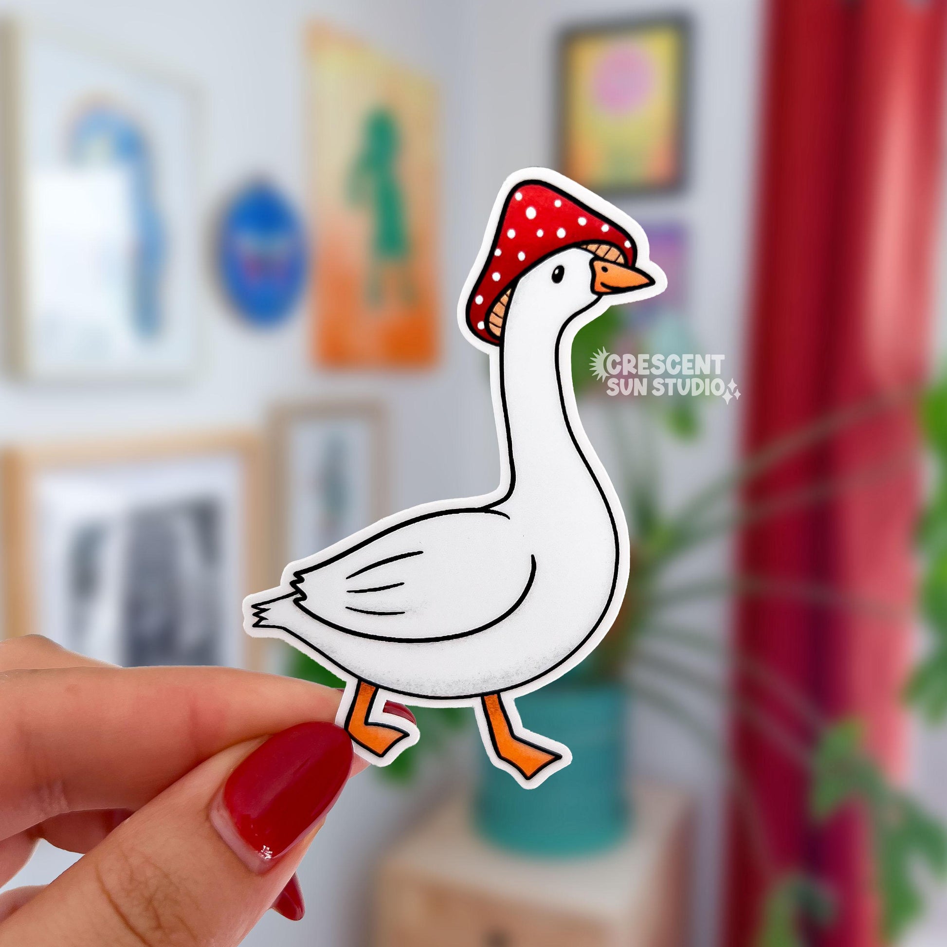 Our goose mushroom sticker features a very silly, but unbothered, white goose wearing a red and white spotted mushroom cap on its head. The sticker shows the white goose's side profile and the bird is also mid-step.
