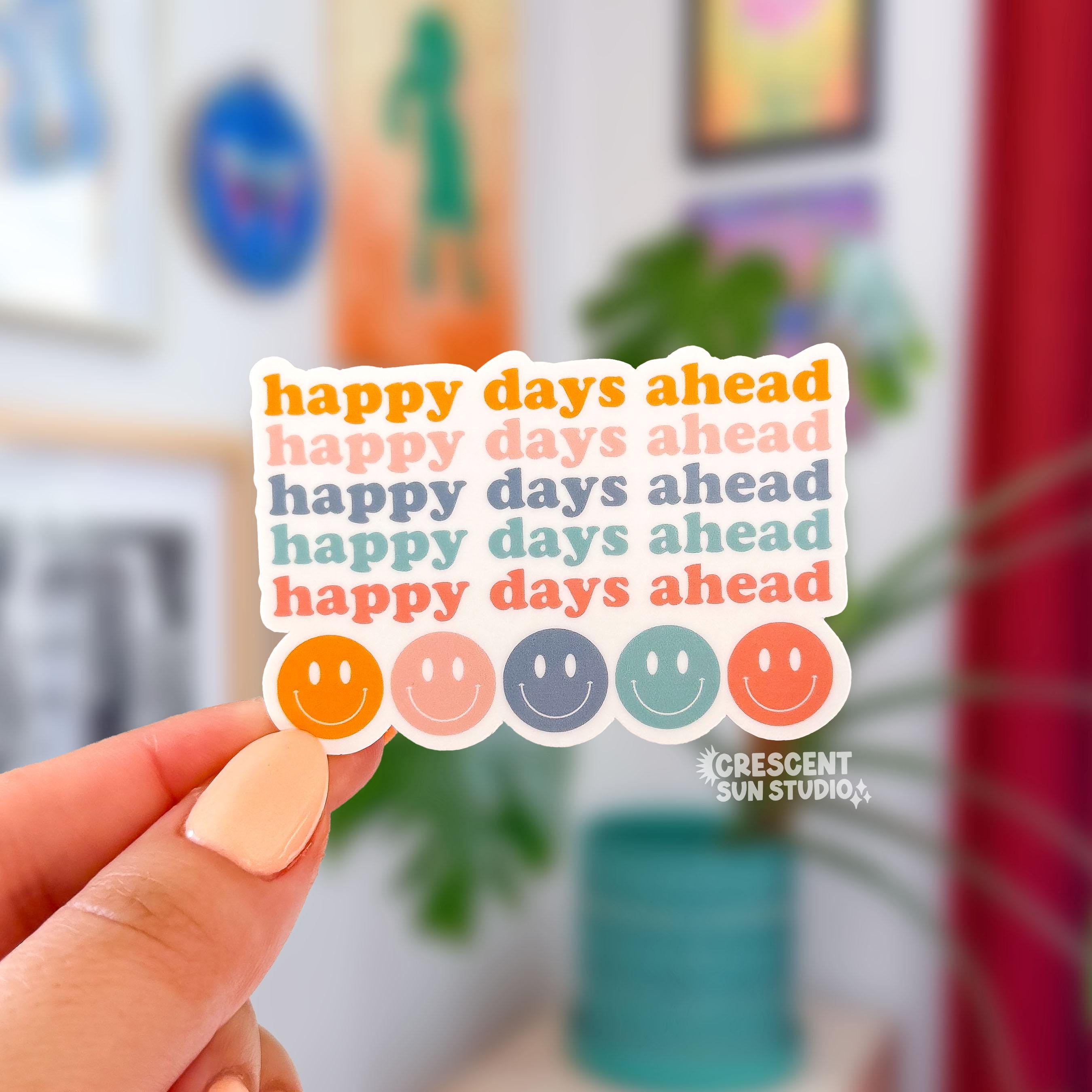 A die cut sticker with 5 lines repeating "happy days ahead" in colors from dark orange, pink, blue, teal, and bright orange. Then there is a row of smiley faces in those same colors.