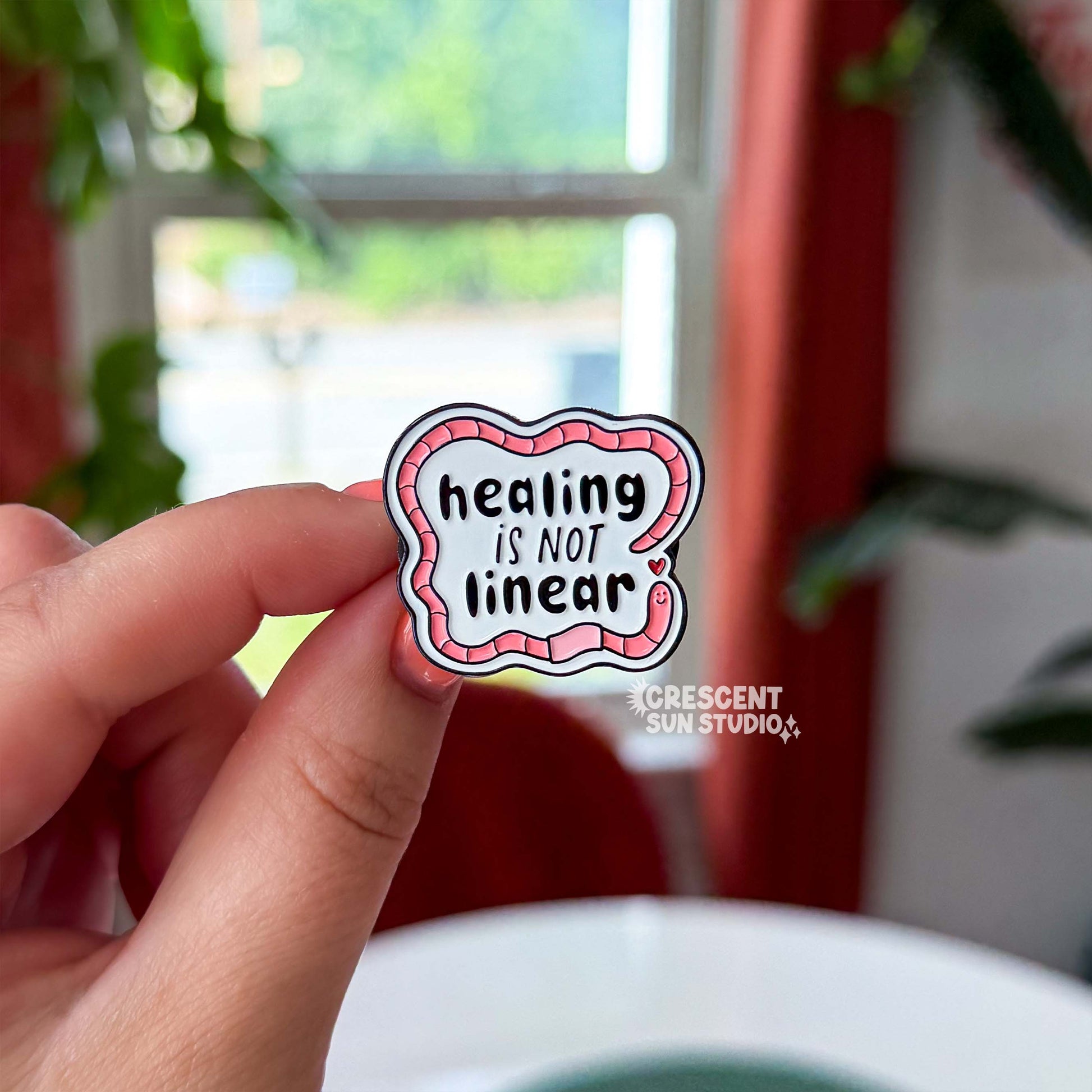The design features bold black text surrounded by a friendly segmented worm. The text reads, "healing is not linear." The worm's head and his tail do not connect, instead, there is a tiny heart separating the two. 