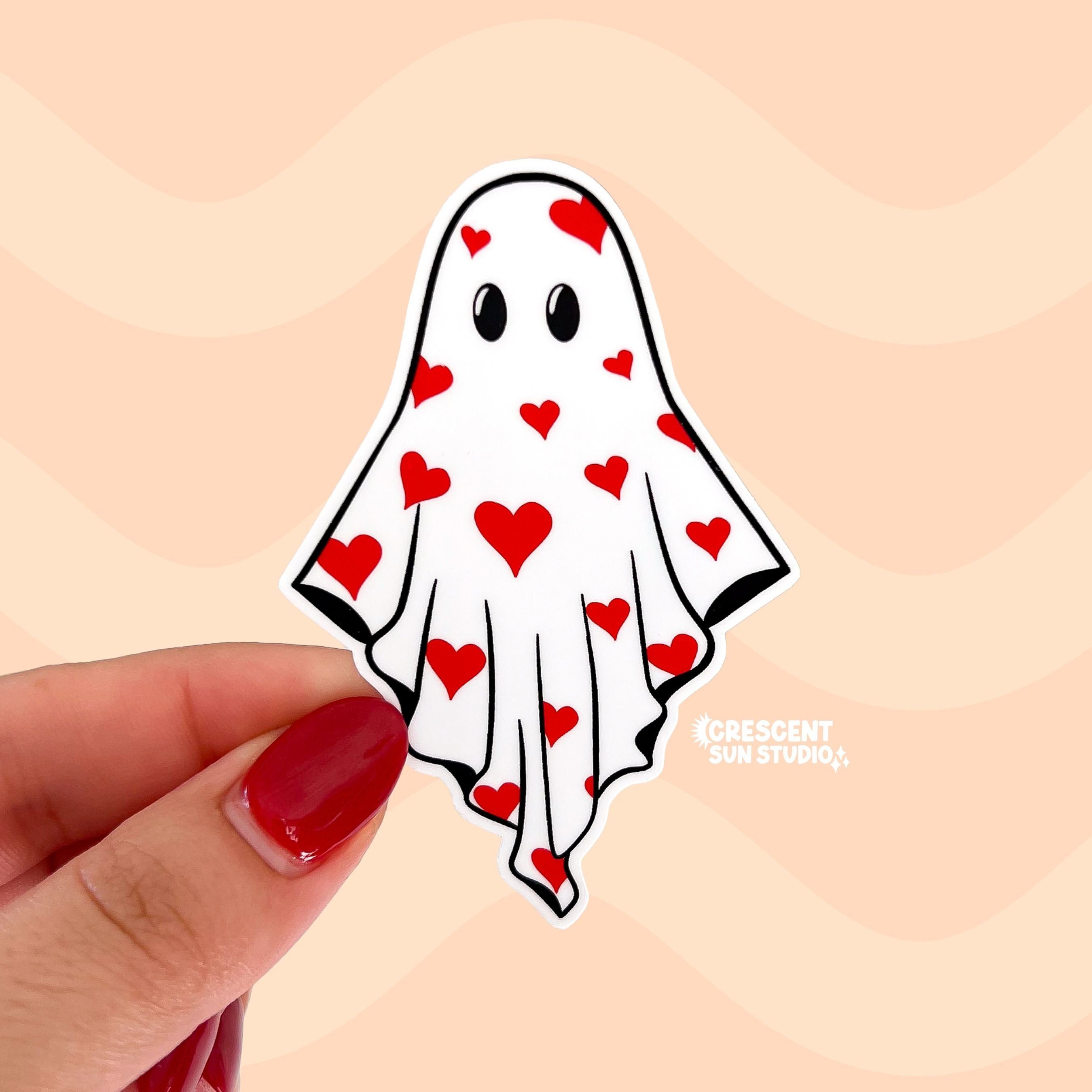 Hand holding a diecut sticker of a ghost with red hearts.