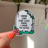 The sticker is in the shape of a light colored tombstone with slight cracks at various points. There is a red flower at the bottom left corner, green green grass, and then a green vine at the top right corner. Written on the gravestone is "here lies the last fuck I had to give" in all caps.

In this image, a hand holds the sticker close to the camera against a light and bright white wall in the background.