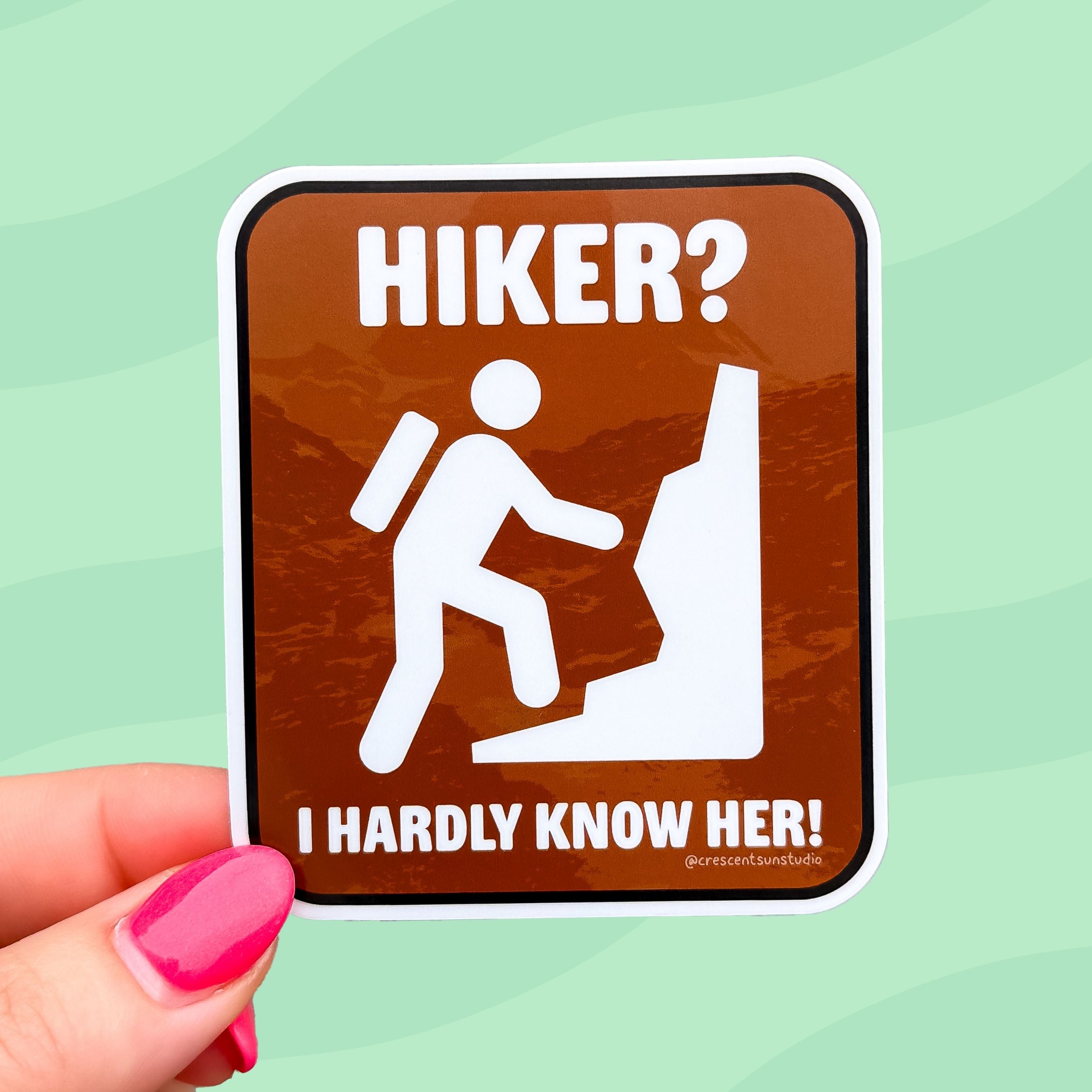 A recreation sign style design features the classic hiking symbol. White text on a brown background reads, "Hiker? I hardly know her." 