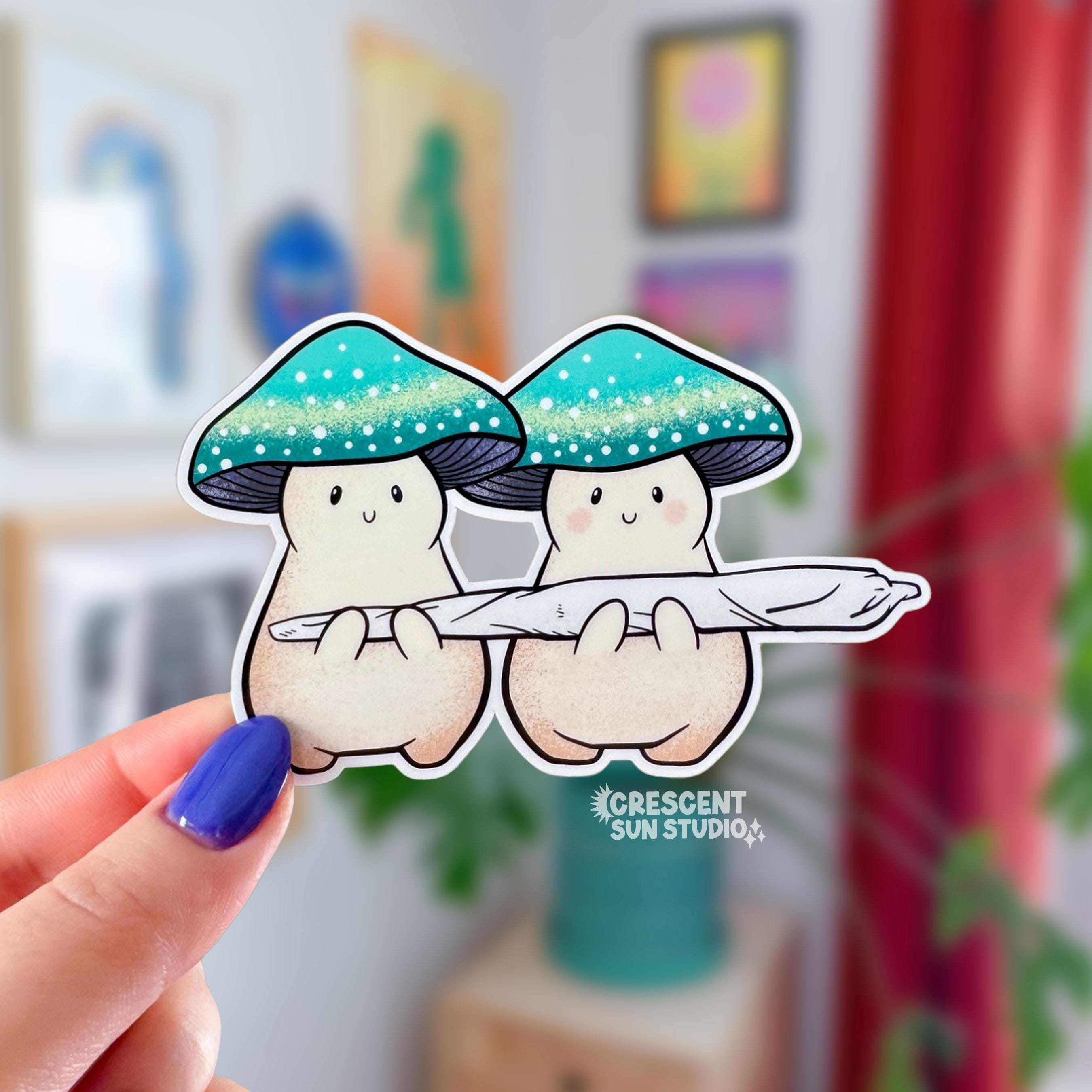 Two cream mushroom characters happily stand next to one another holding a giant joint that is larger than the two of them together! One mushroom has slightly rosier cheeks than the other. Both characters have a green mushroom cap and towards the bottom, the caps have a band of yellow and white dots that give a sparkle effect.

In this image, a hand holds a sticker version of the pair close to the camera.