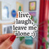 A die-cut sticker (follows the shape of the words) that reads "live, laugh, leave me alone" on four lines in black text on a white background. At the end of the text there is a smiley face emoticon. 