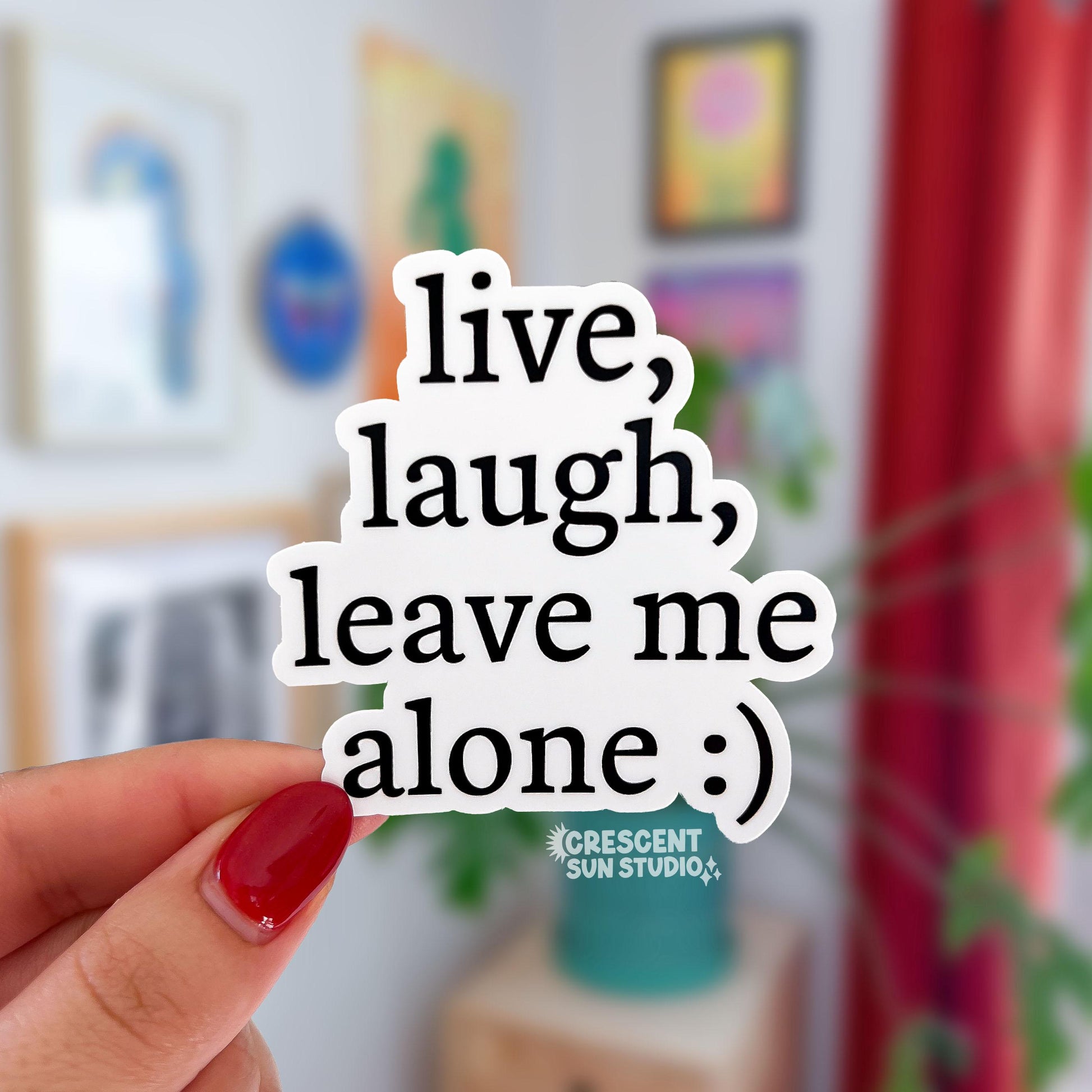 A die-cut sticker (follows the shape of the words) that reads "live, laugh, leave me alone" on four lines in black text on a white background. At the end of the text there is a smiley face emoticon. 