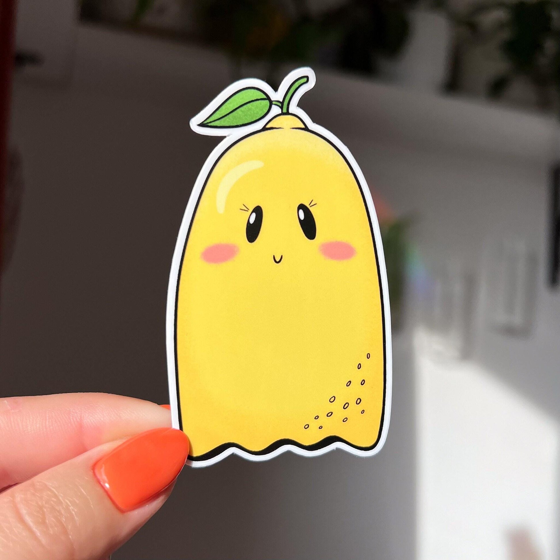 Imagine a sticker in the shape of a ghost, but also a lemon! With a little green leafy stem atop its yellow body, this ghost has a subtle smile, rosy cheeks, and eyelashes.