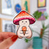 A mushroom character sticker whose cap is colored in stripes of orange, white, and pink. The mushroom is holding an orange ice cream cone.